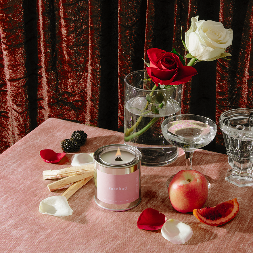 Candle, flowers, and fruit on a table with a red curtain background