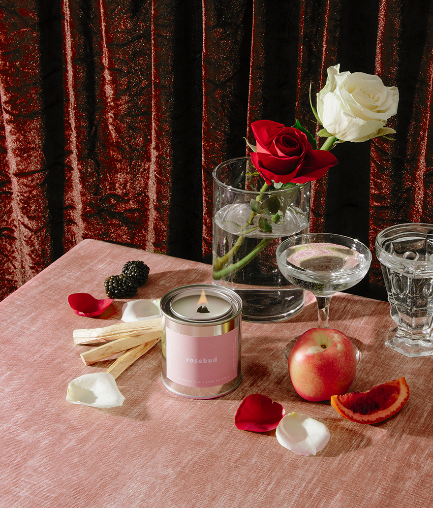 Candle, flowers, and fruit on a table with a red curtain background