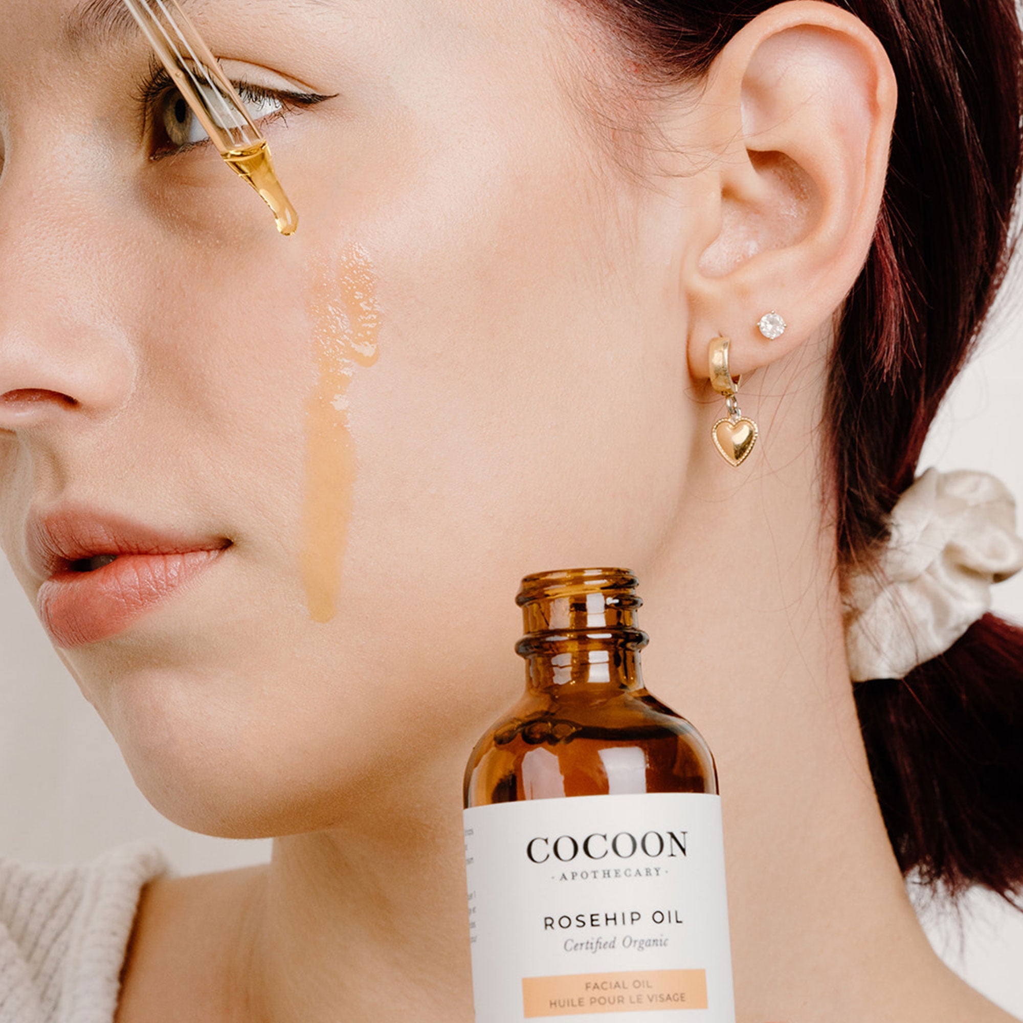 Woman applying Cocoon Rosehip Oil to her face with a dropper.