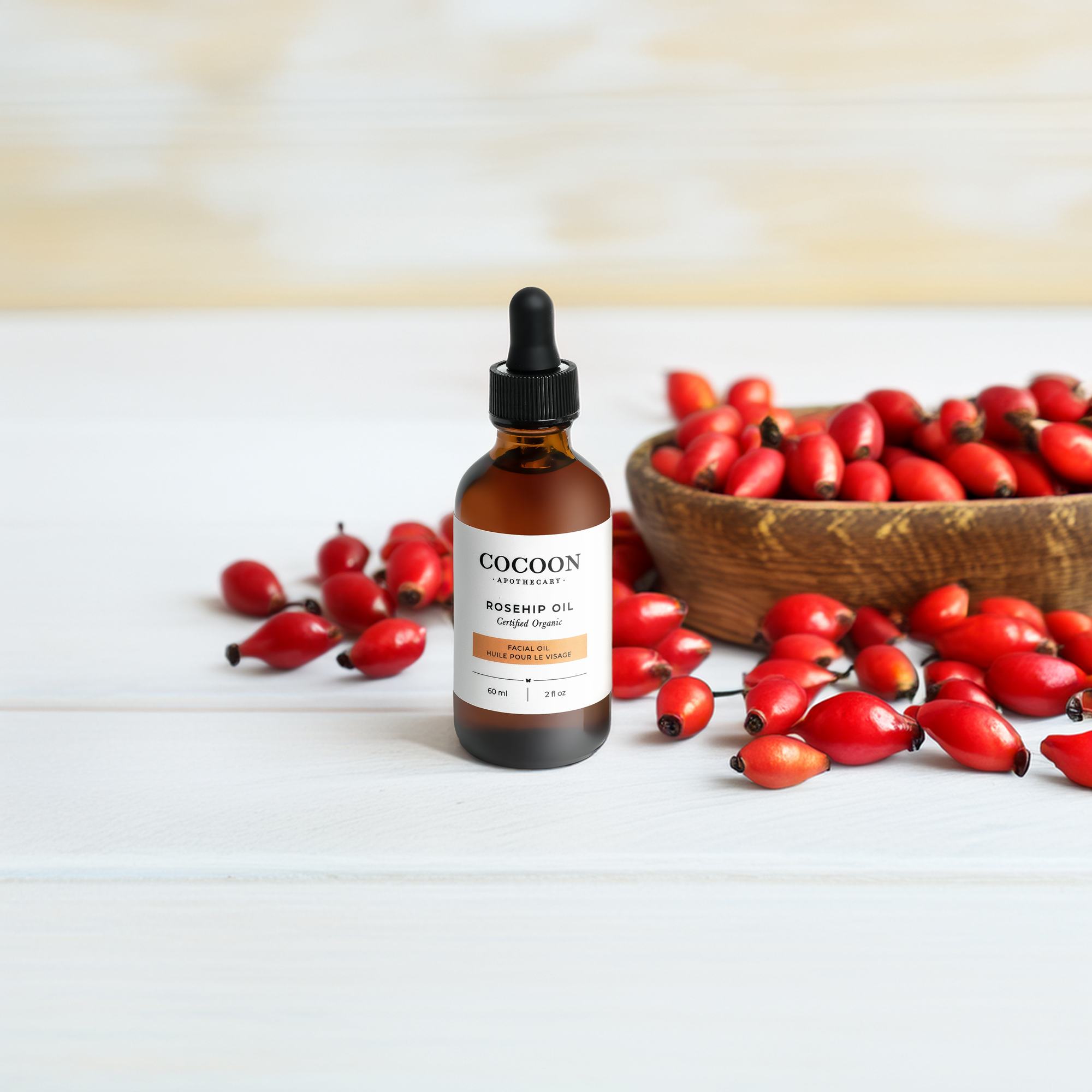 Bottle of Cocoon Rosehip Oil with rosehips on a wooden surface