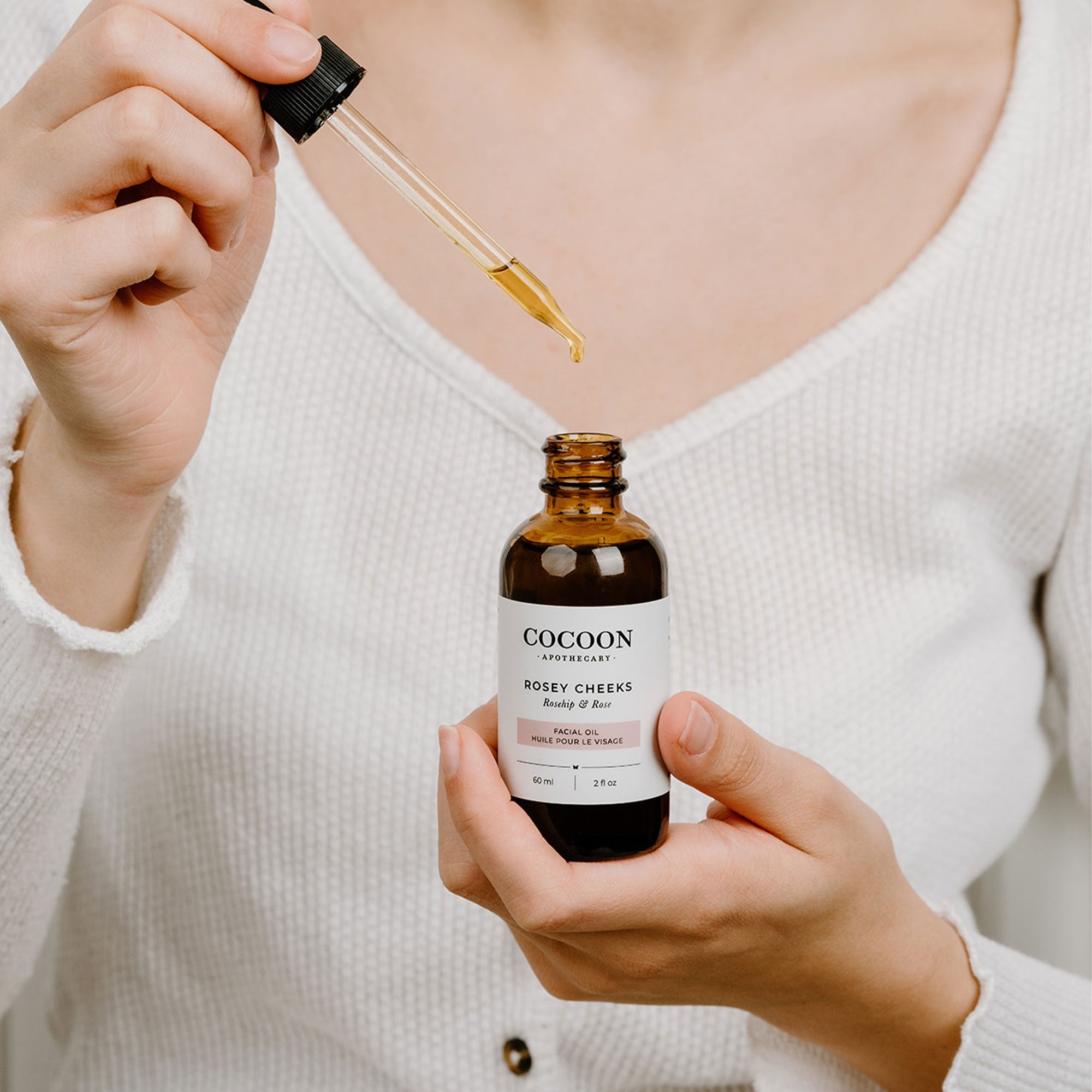 Person holding a bottle of Cocoon skincare product with a dropper.