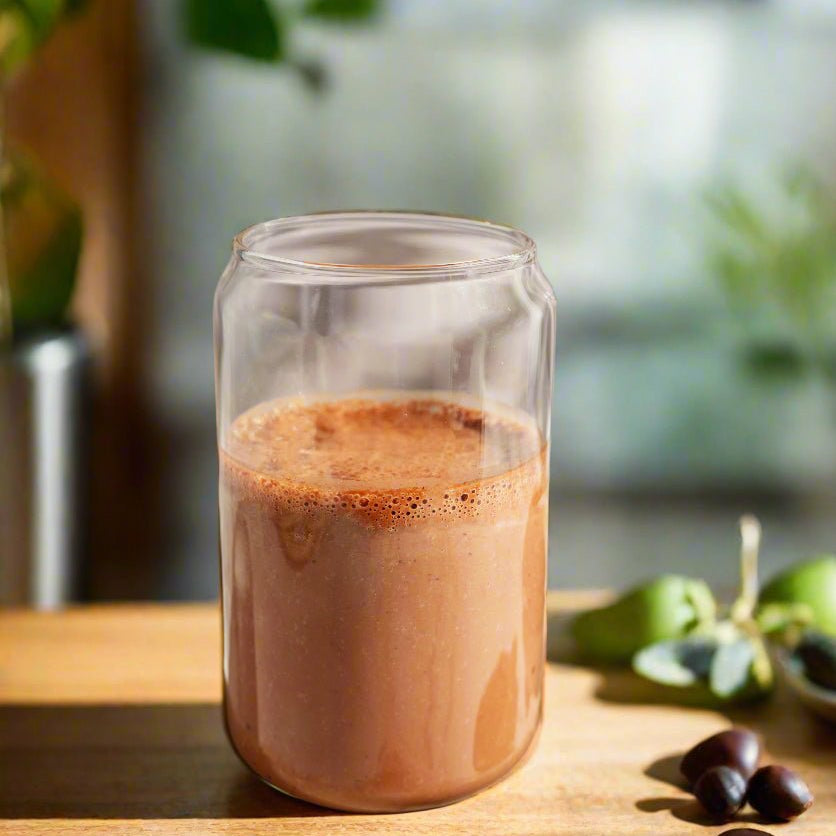 Glass of chocolate milk on a wooden surface with greenery in the background