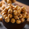 Bowl of popcorn on a dark surface with a wooden board in the background sea salt and maple coating from Toronto Popcorn company