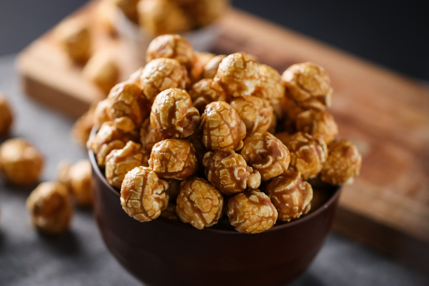 Bowl of popcorn on a dark surface with a wooden board in the background sea salt and maple coating from Toronto Popcorn company