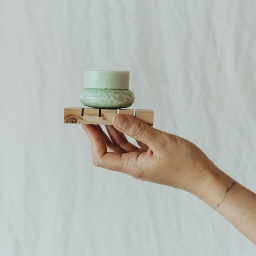 Hand holding a small green ceramic bowl on a wooden block against a plain background