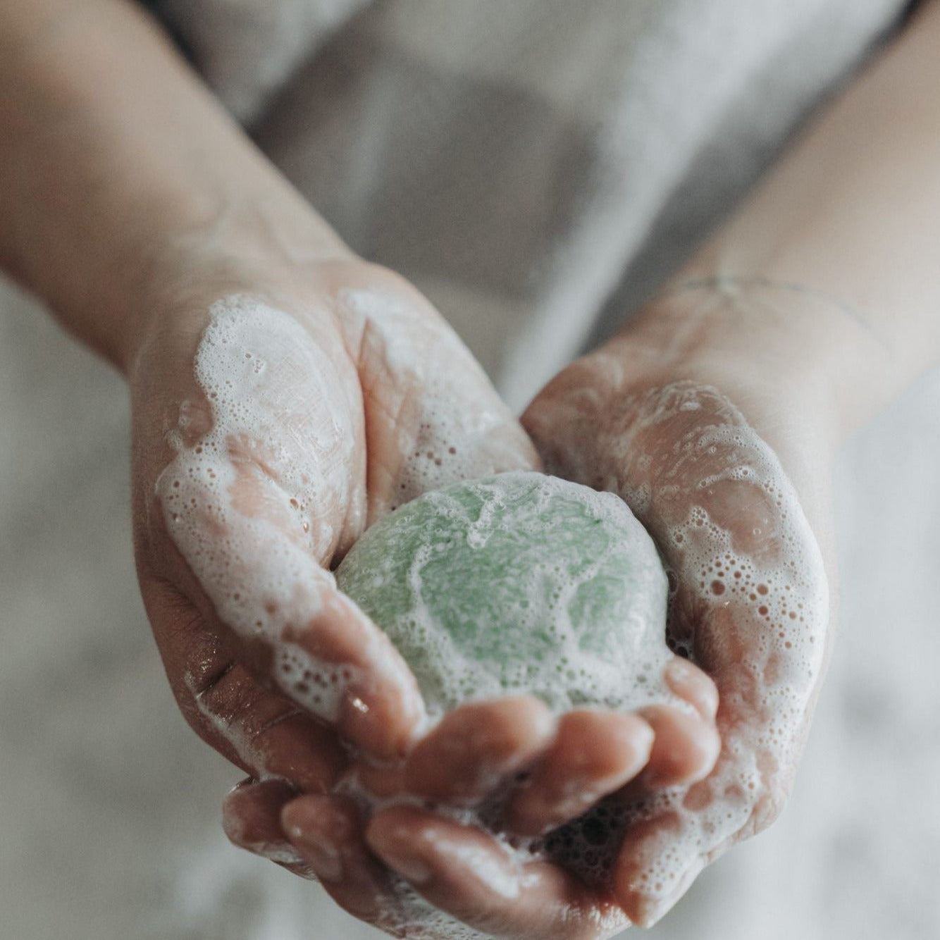 Hands holding a green soap bar with foam, against a neutral background