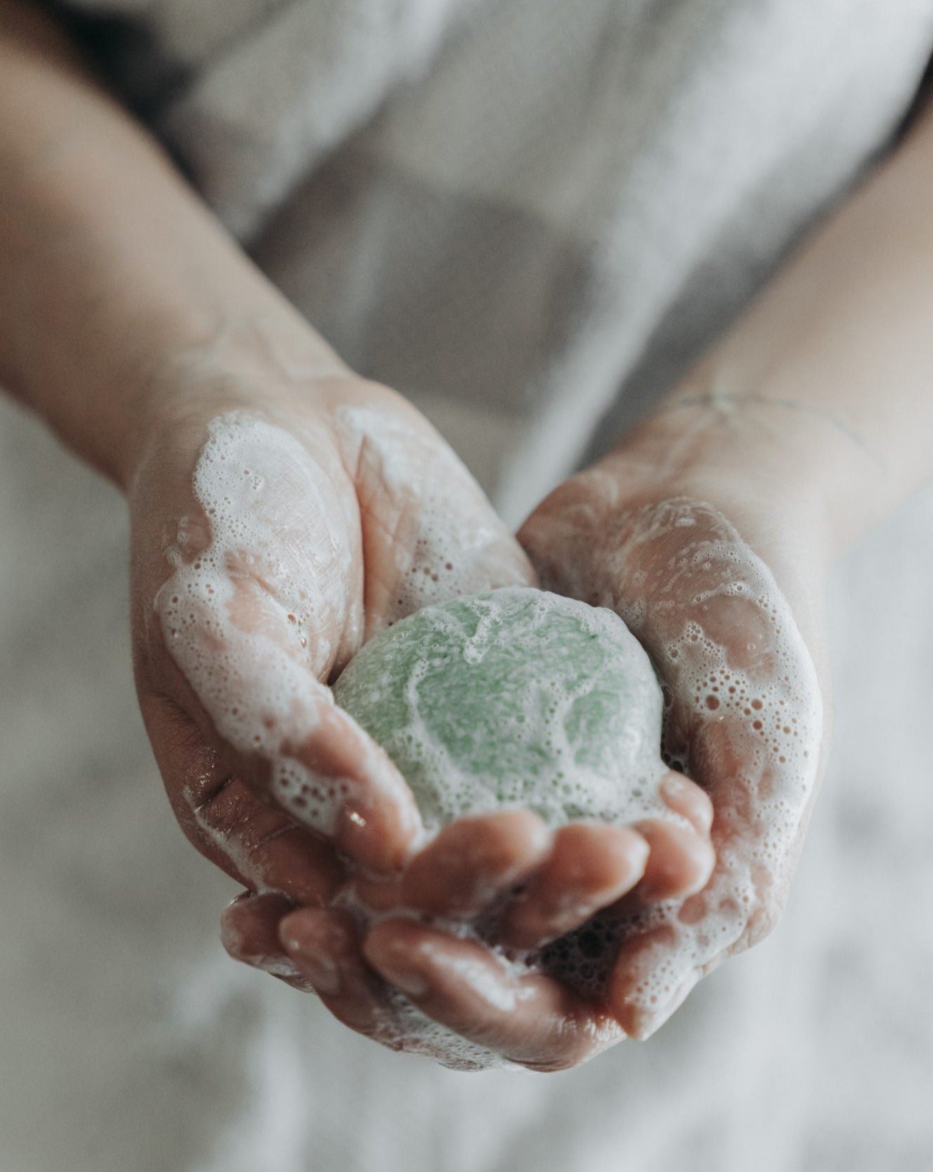 Hands holding a green soap bar with foam, against a neutral background