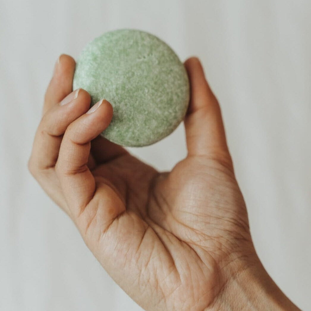 Hand holding a green bath bomb against a plain background