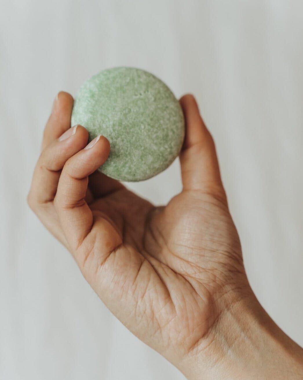 Hand holding a green bath bomb against a plain background