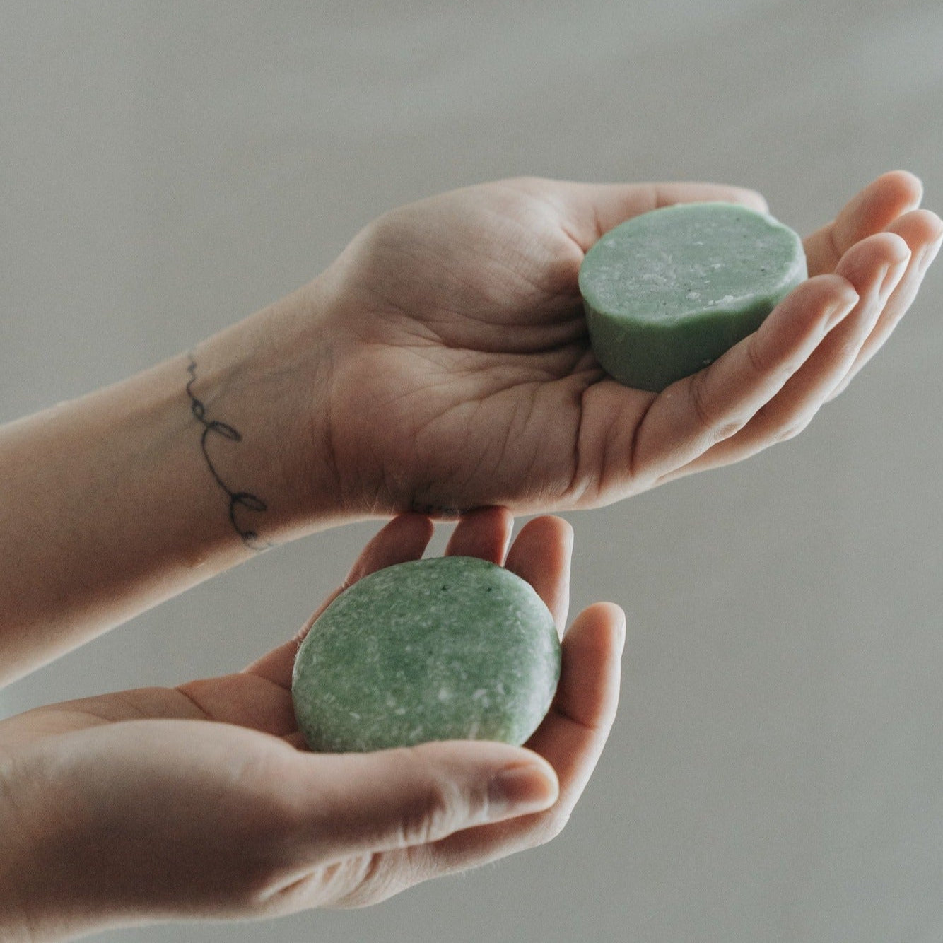 Two hands holding green soap bars against a neutral background