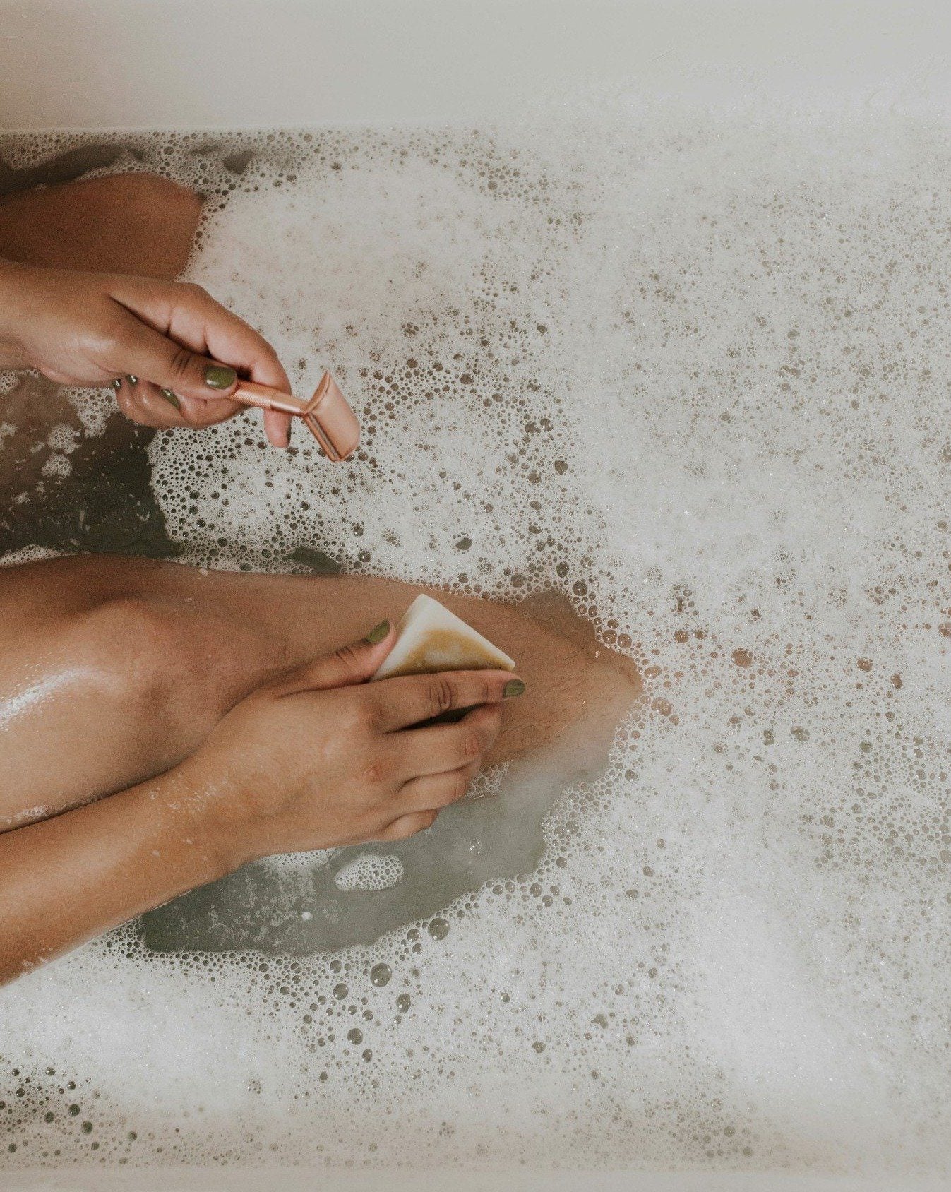 Person scrubbing feet with a washcloth in a bathtub filled with bubbles