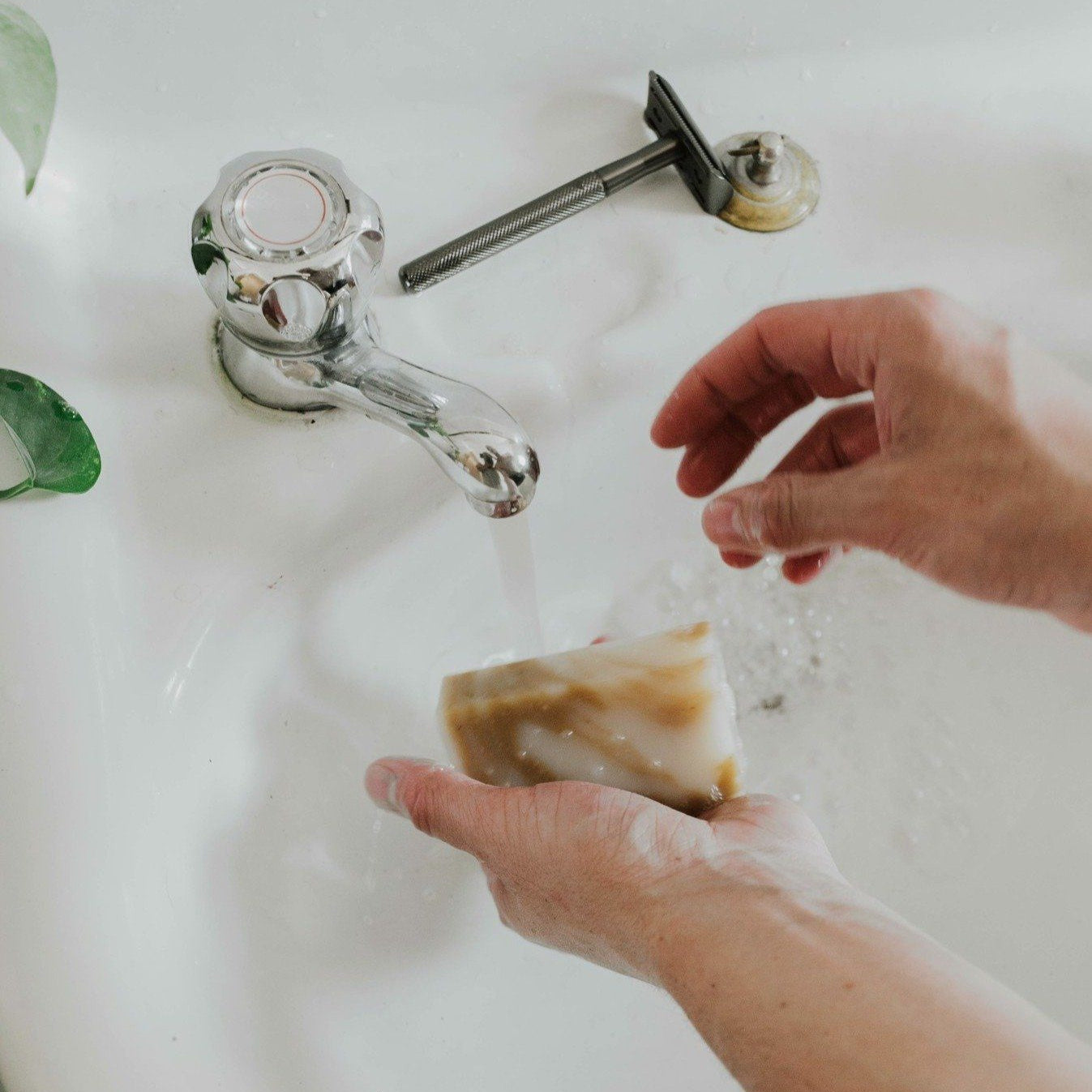 Person washing a bar of soap under running water from a faucet.