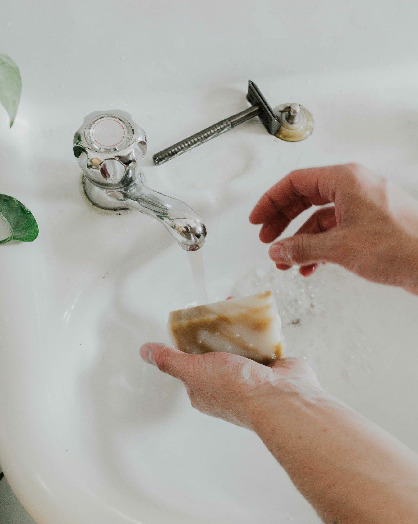Person washing a bar of soap under running water from a faucet.