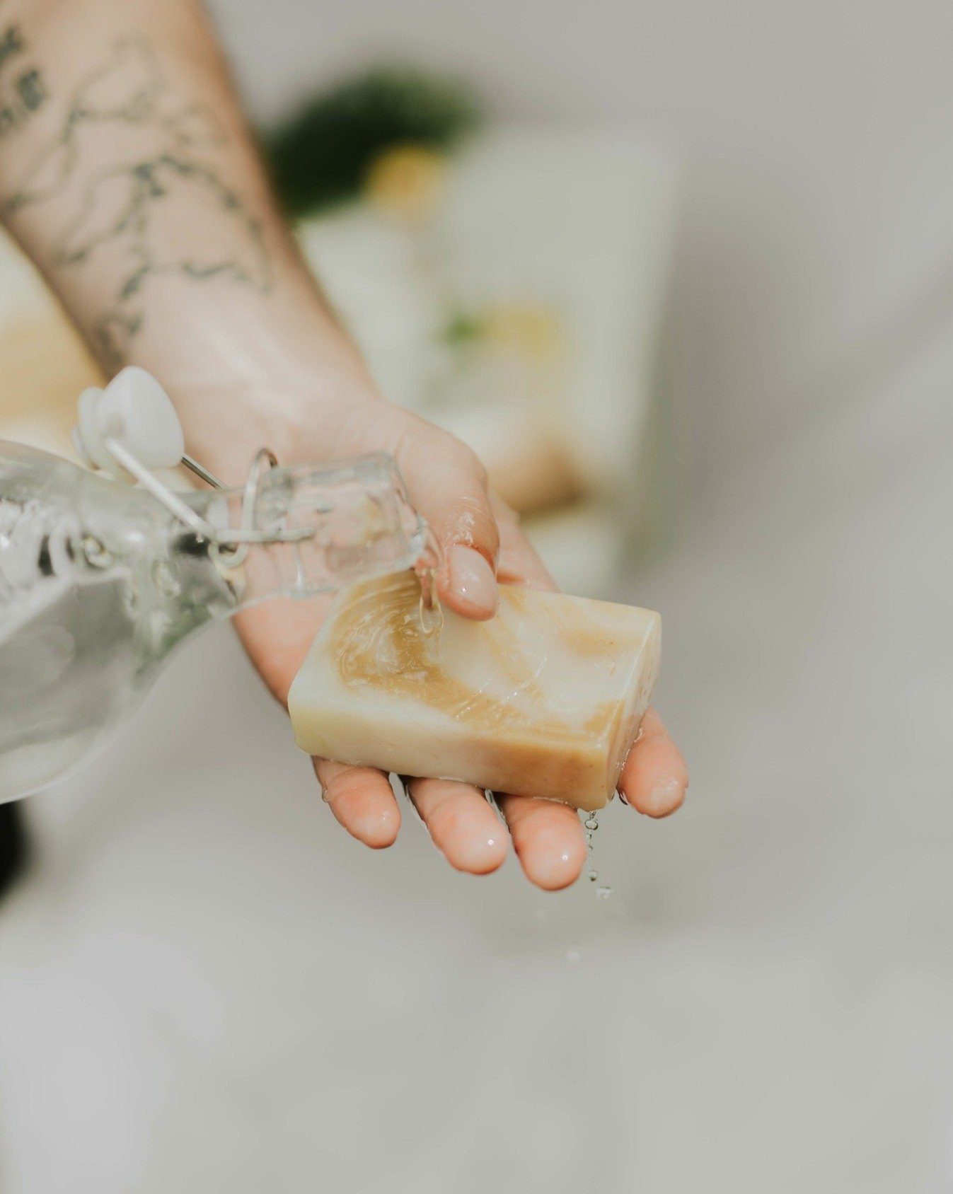 Hand holding a bar of soap with water droplets, blurred background