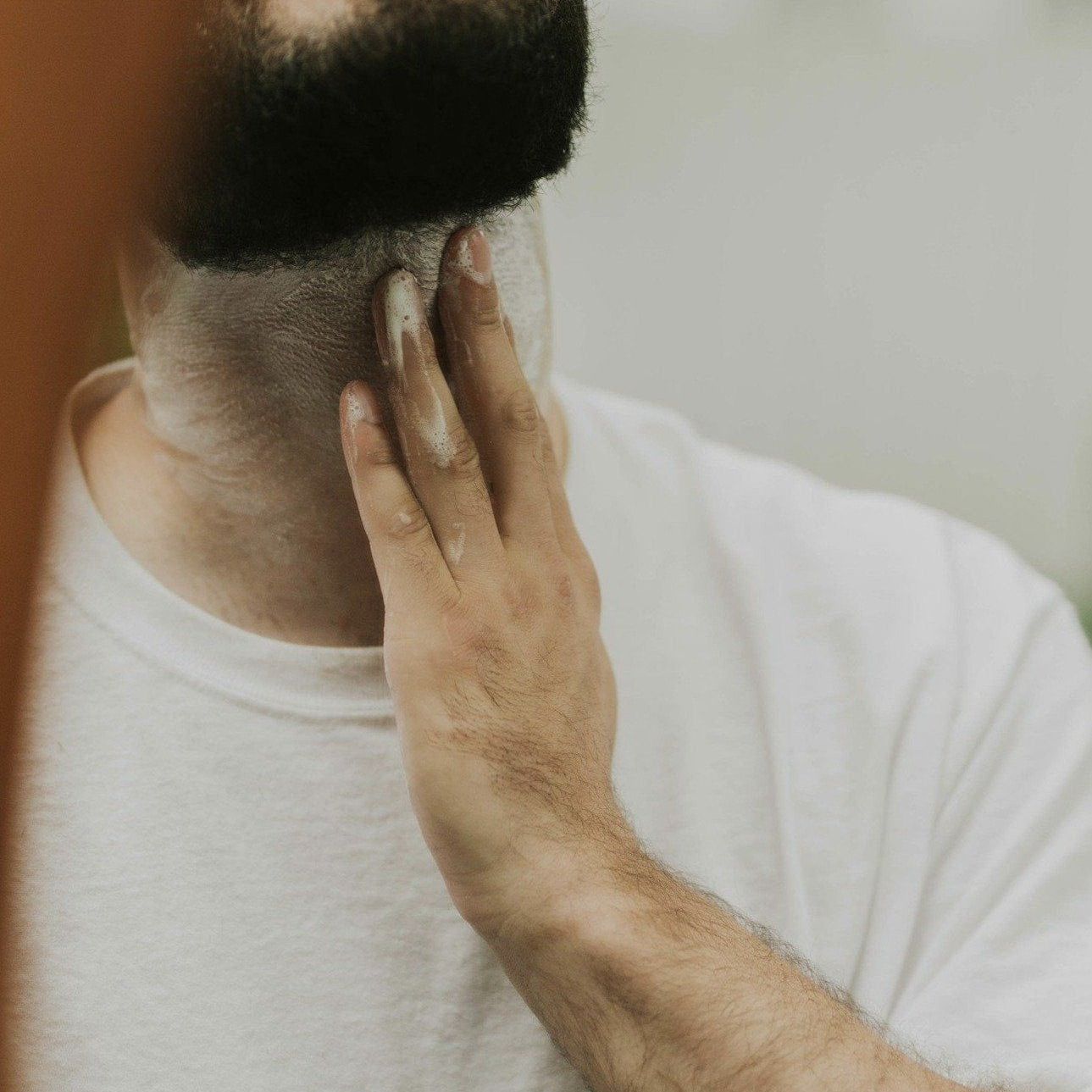 Man with a beard touching his face in front of a mirror