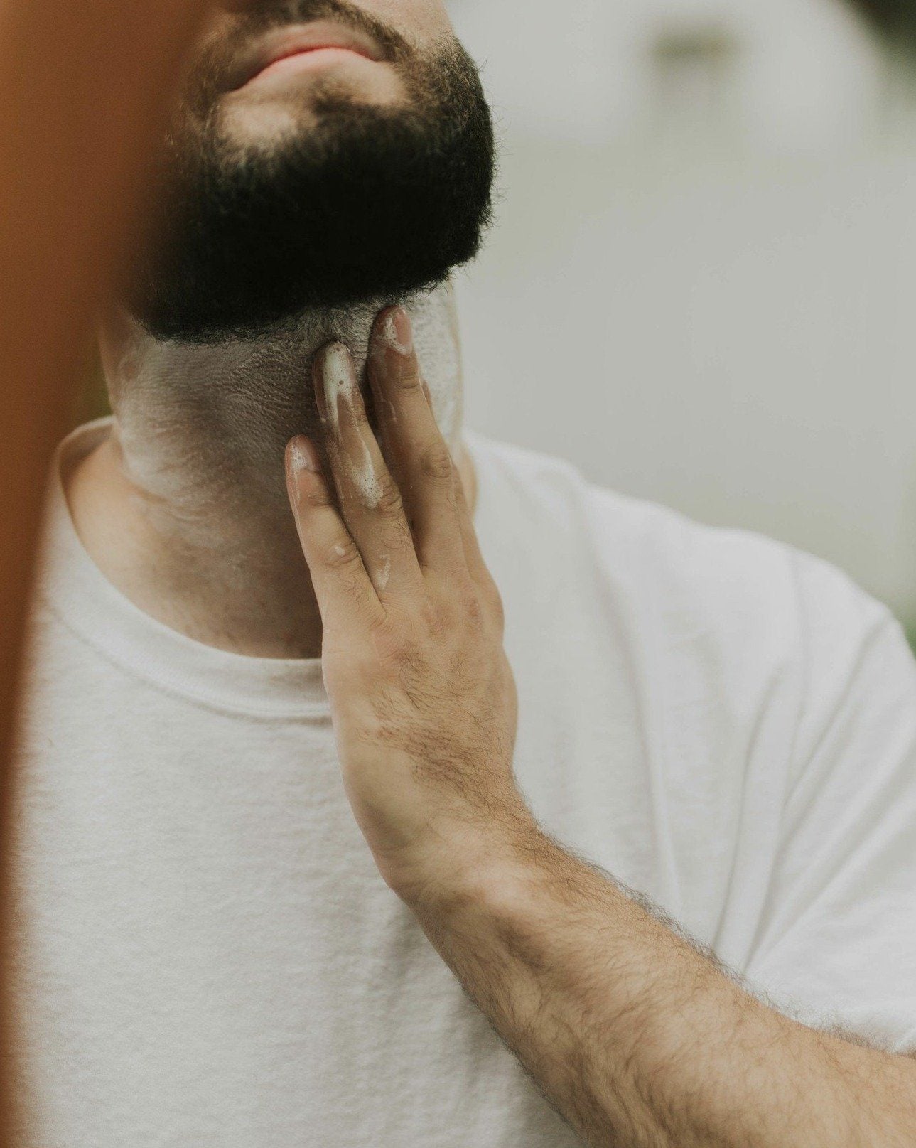 Man with a beard touching his face in front of a mirror