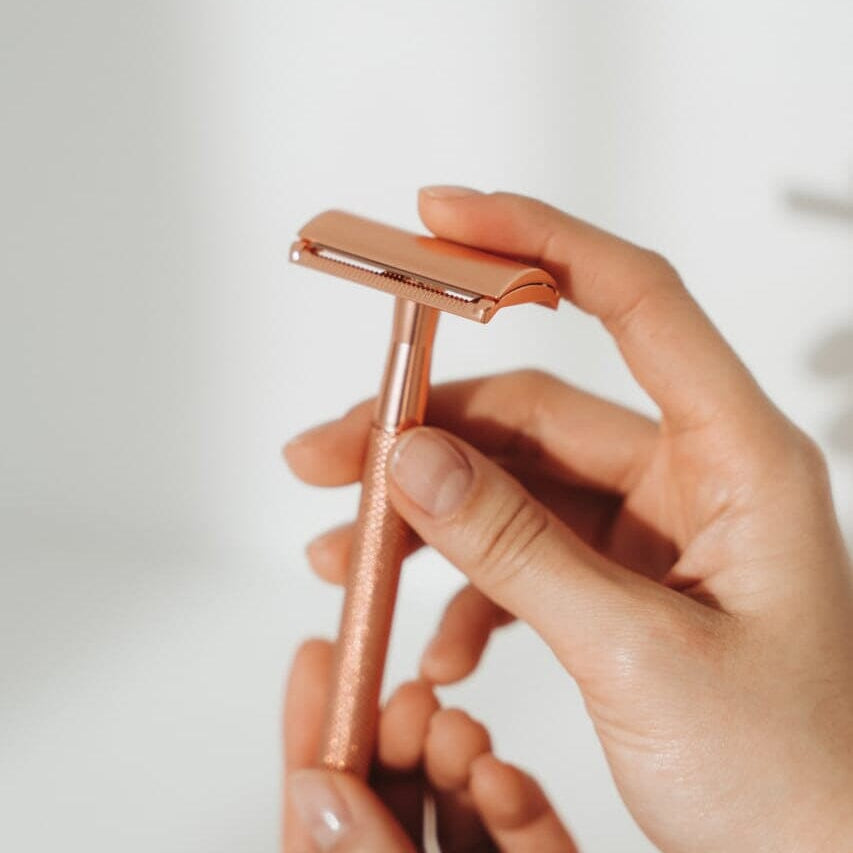 Rose gold safety razor held by a hand against a light background