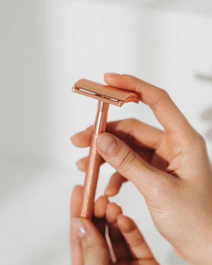 Rose gold safety razor held by a hand against a light background