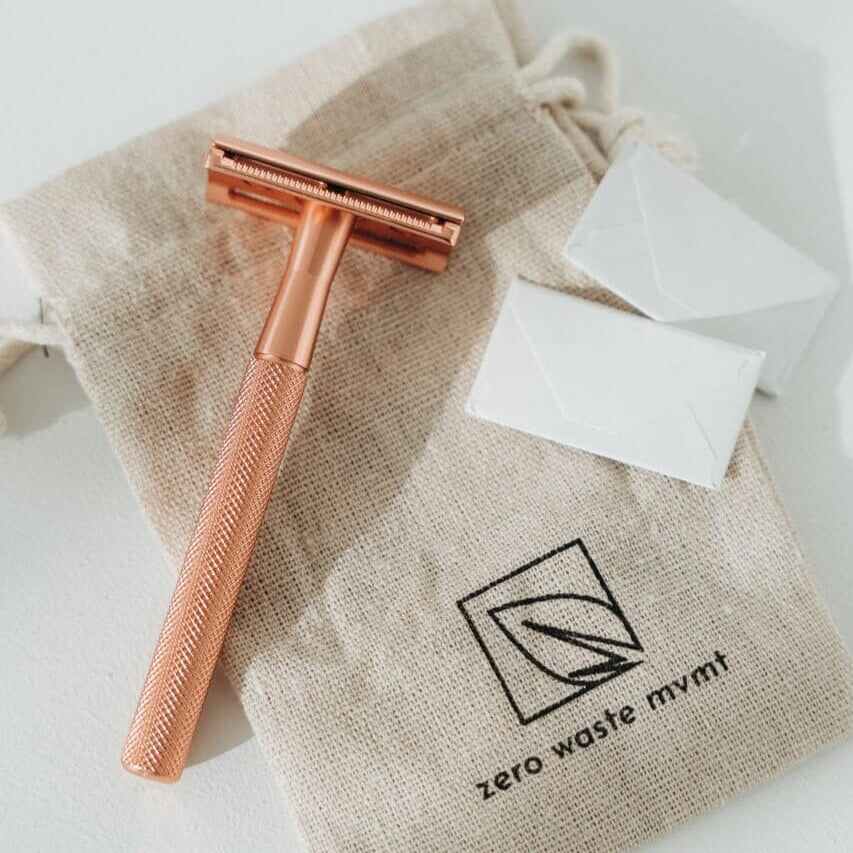 Rose gold razor with white cartridges on a beige drawstring bag labeled 'zero waste mym'.