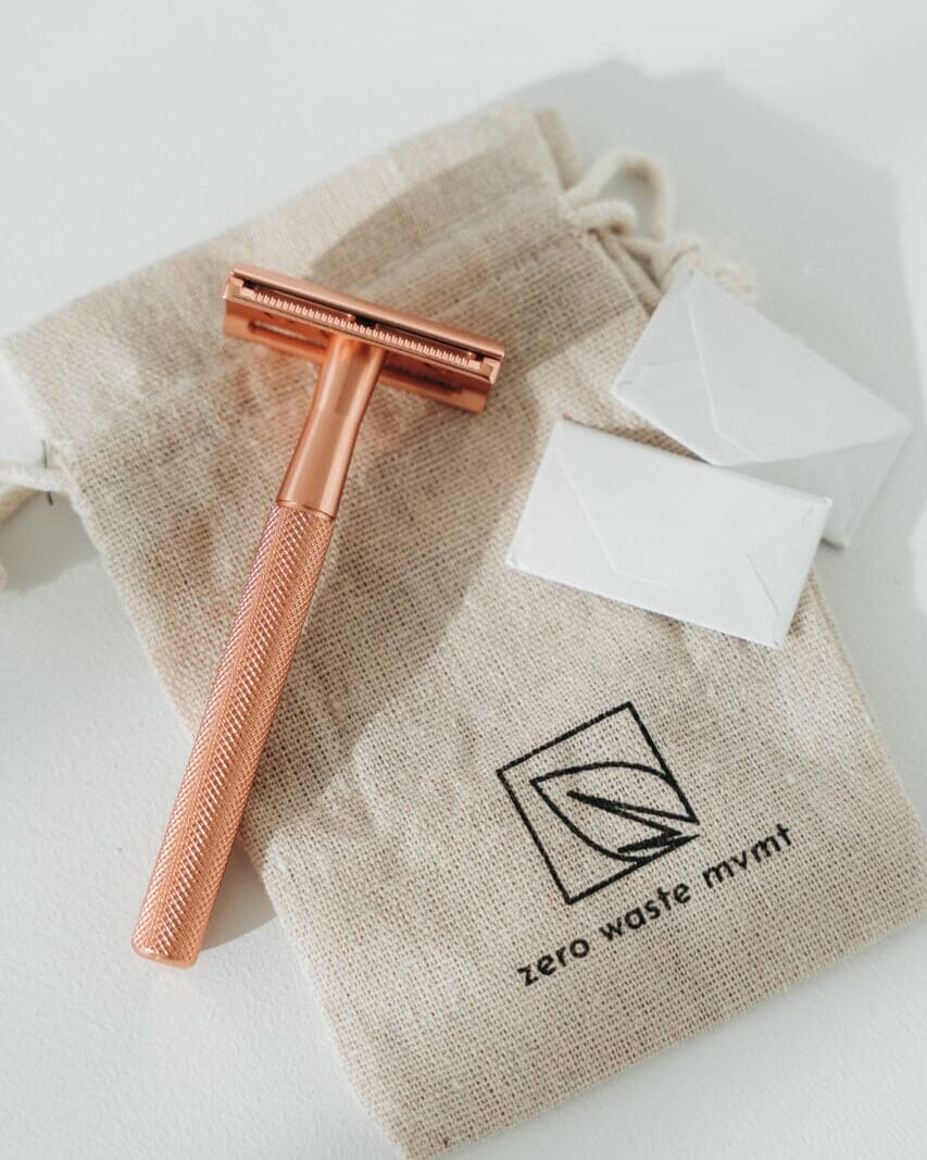 Rose gold razor with white cartridges on a beige drawstring bag labeled 'zero waste mym'.