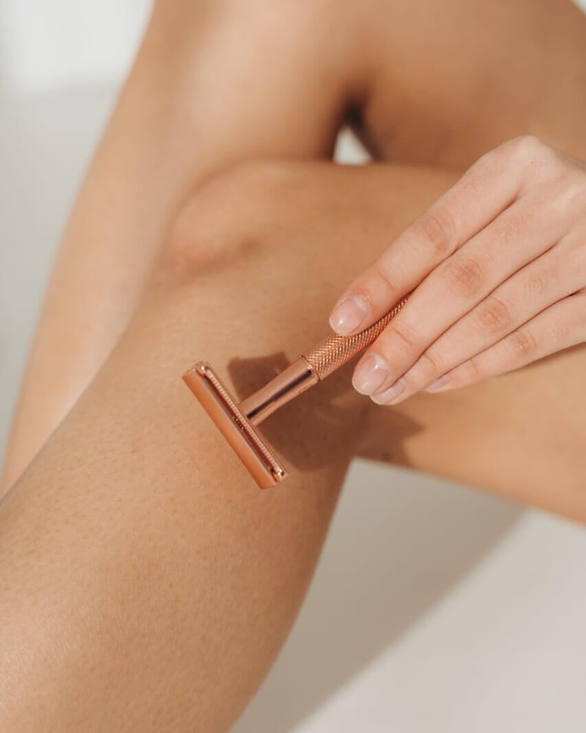 Person using a rose gold safety razor on their arm against a neutral background