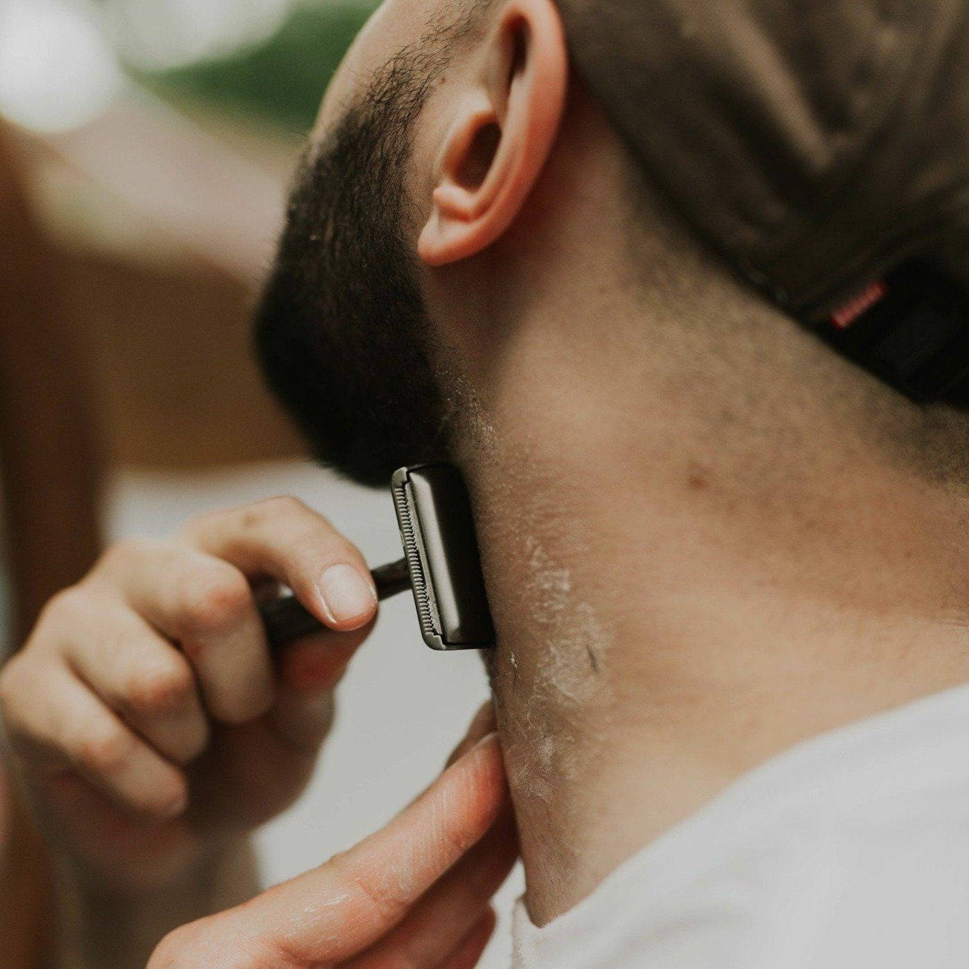 Person shaving their neck with a razor outdoors