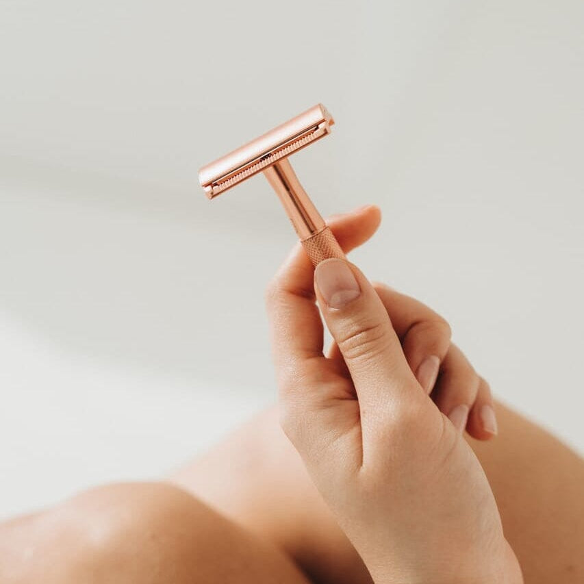 Rose gold safety razor held by a hand against a neutral background