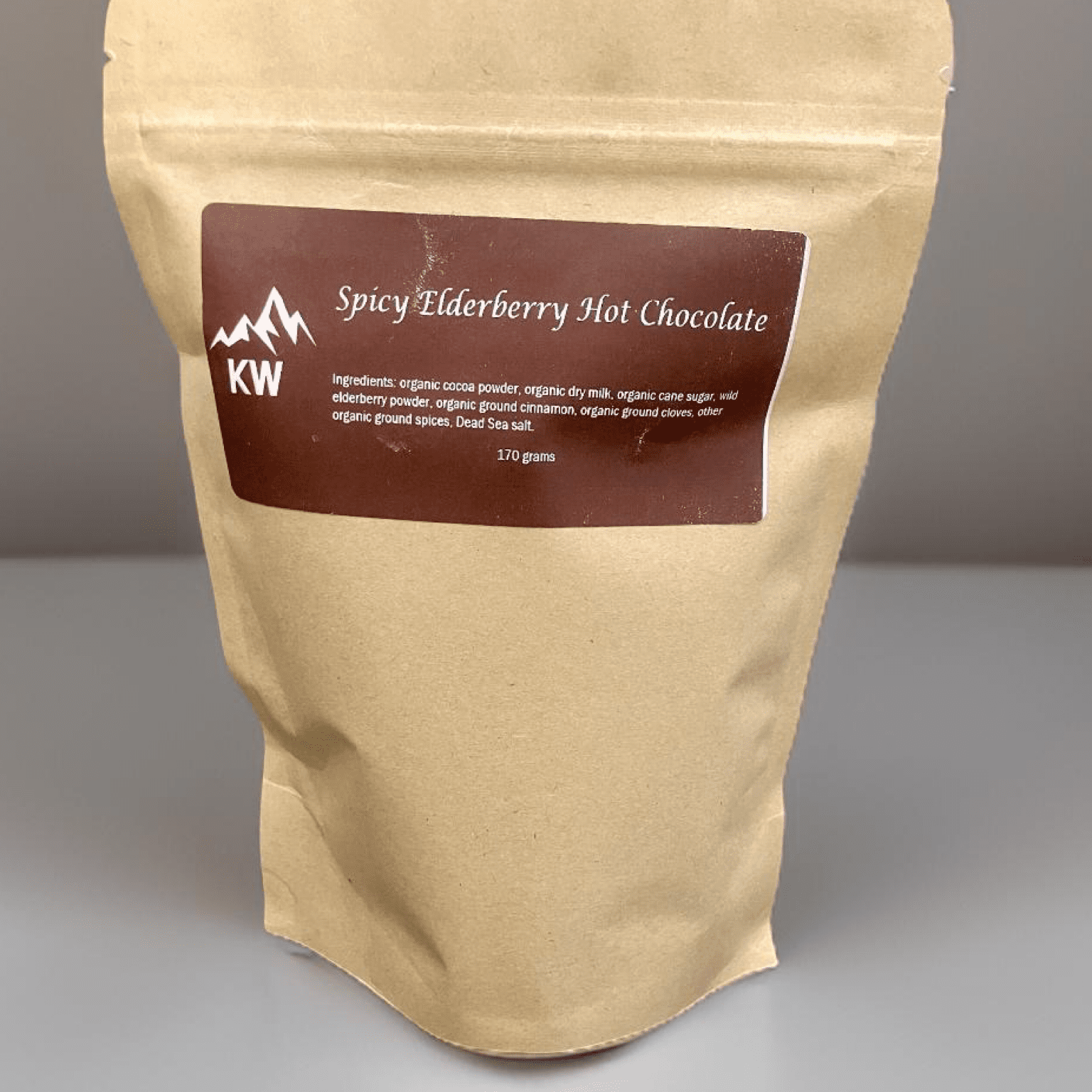 Kraft paper packaging of Spicy Elderberry Hot Chocolate with a brown label on a gray background