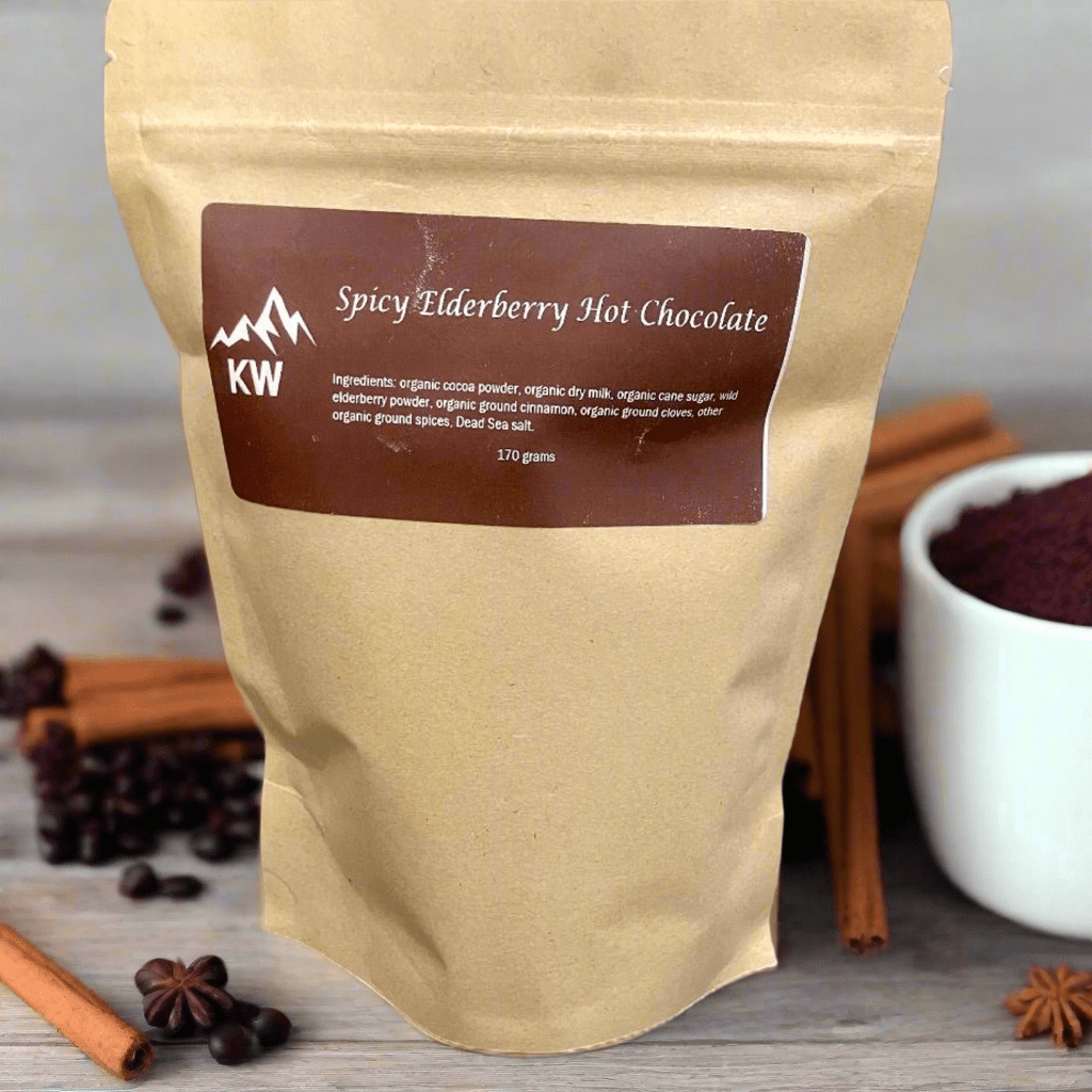 Kraft paper package of Spicy Elderberry Hot Chocolate with a brown label, surrounded by cinnamon sticks and star anise on a wooden surface.