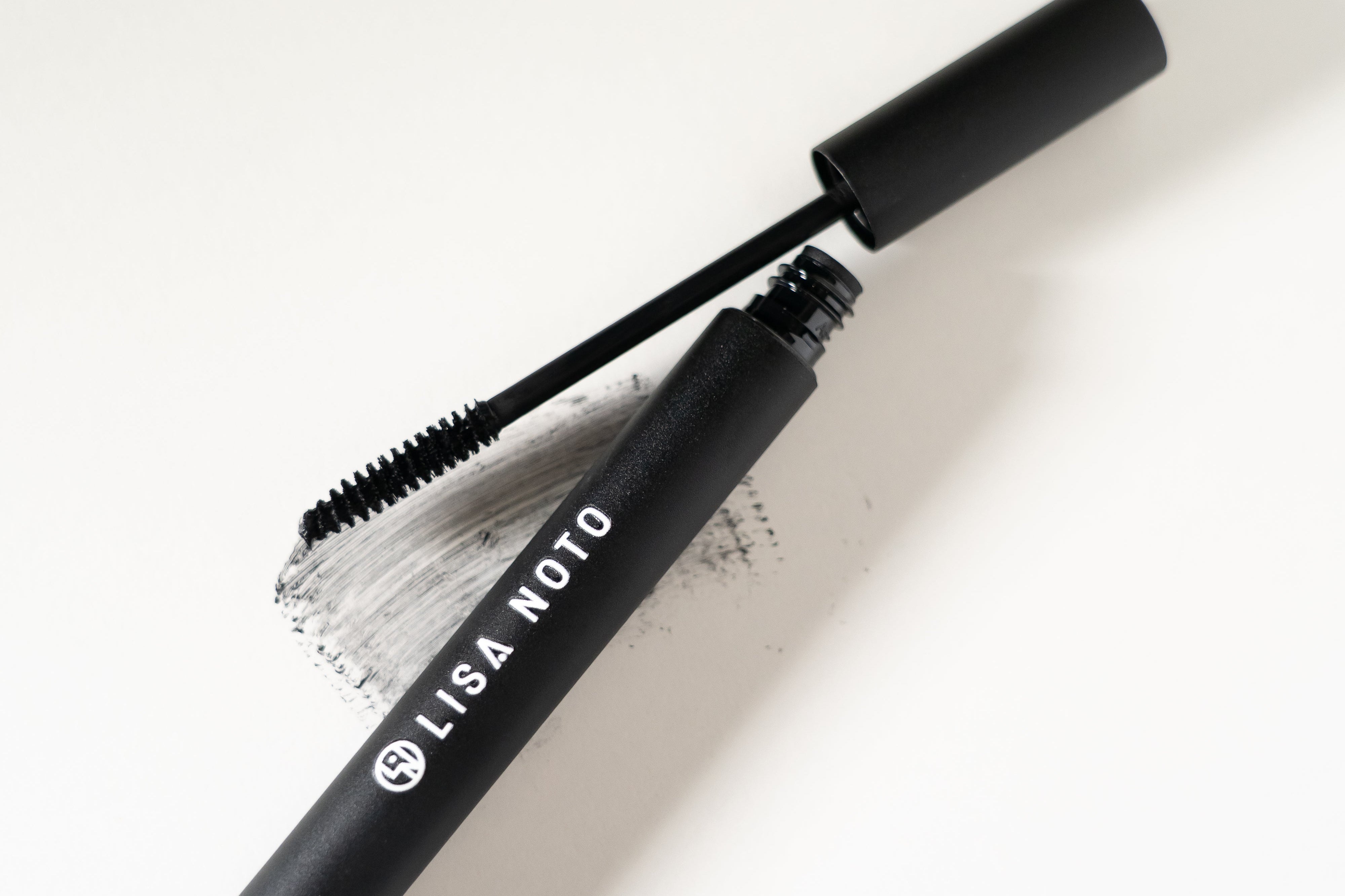 LISA NOTO Volumizing Natural Mascara black tube of mascara with its wand applicator resting beside it on a clean white background. The tube is labeled 'LISA NOTO' in white text.