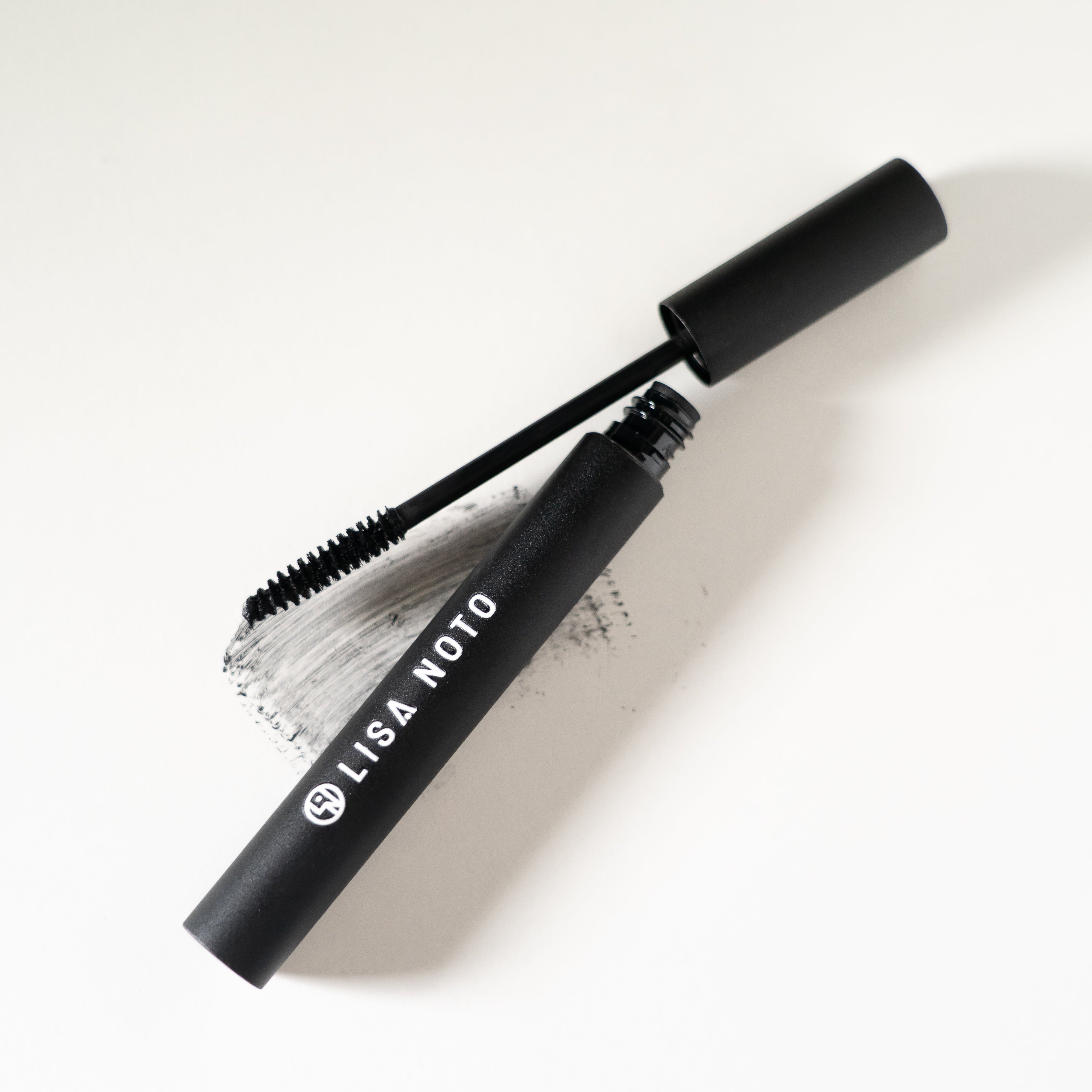 LISA NOTO Volumizing Natural Mascara black tube of mascara with its wand applicator resting beside it on a clean white background. The tube is labeled 'LISA NOTO' in white text.