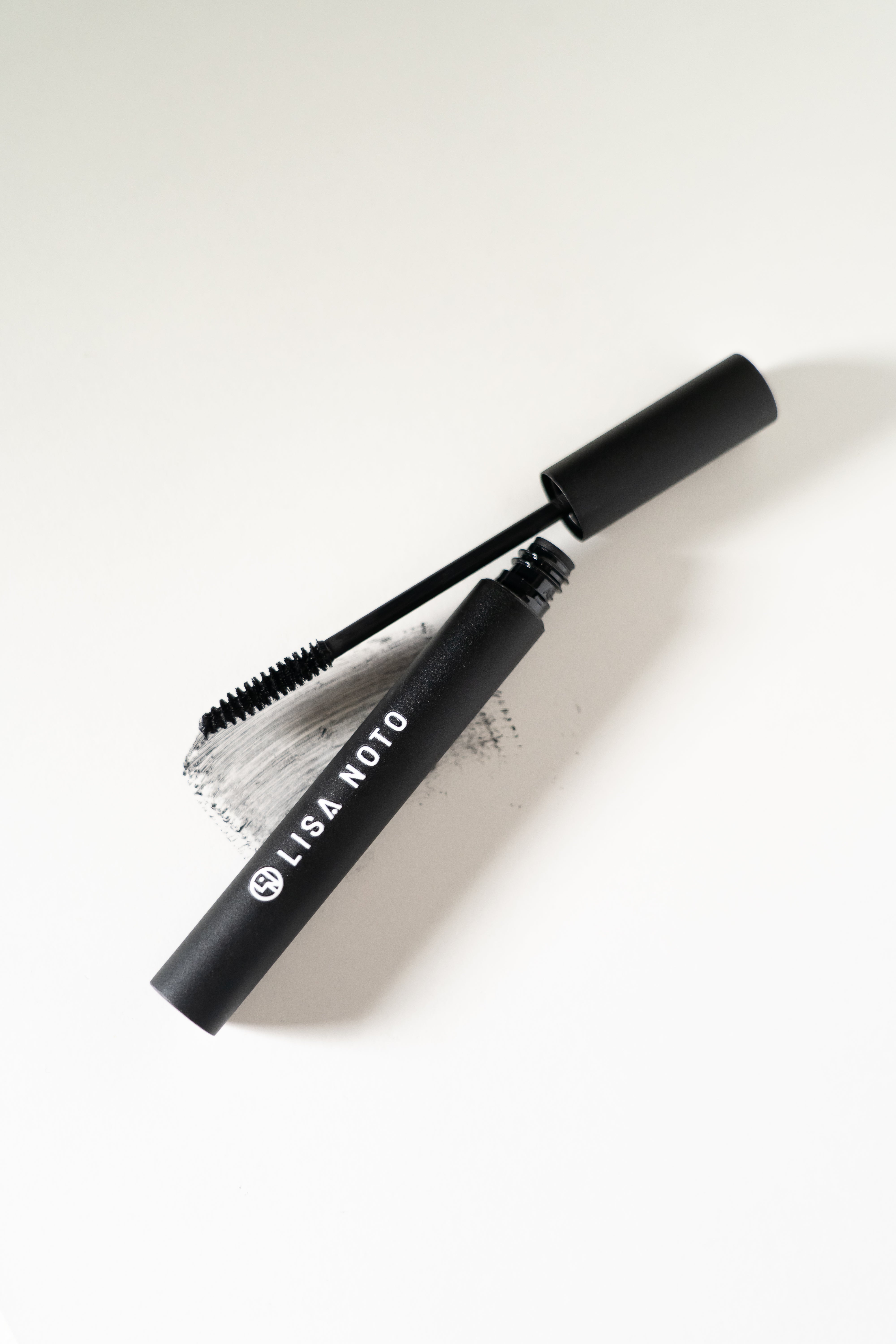 LISA NOTO Volumizing Natural Mascara black tube of mascara with its wand applicator resting beside it on a clean white background. The tube is labeled 'LISA NOTO' in white text.