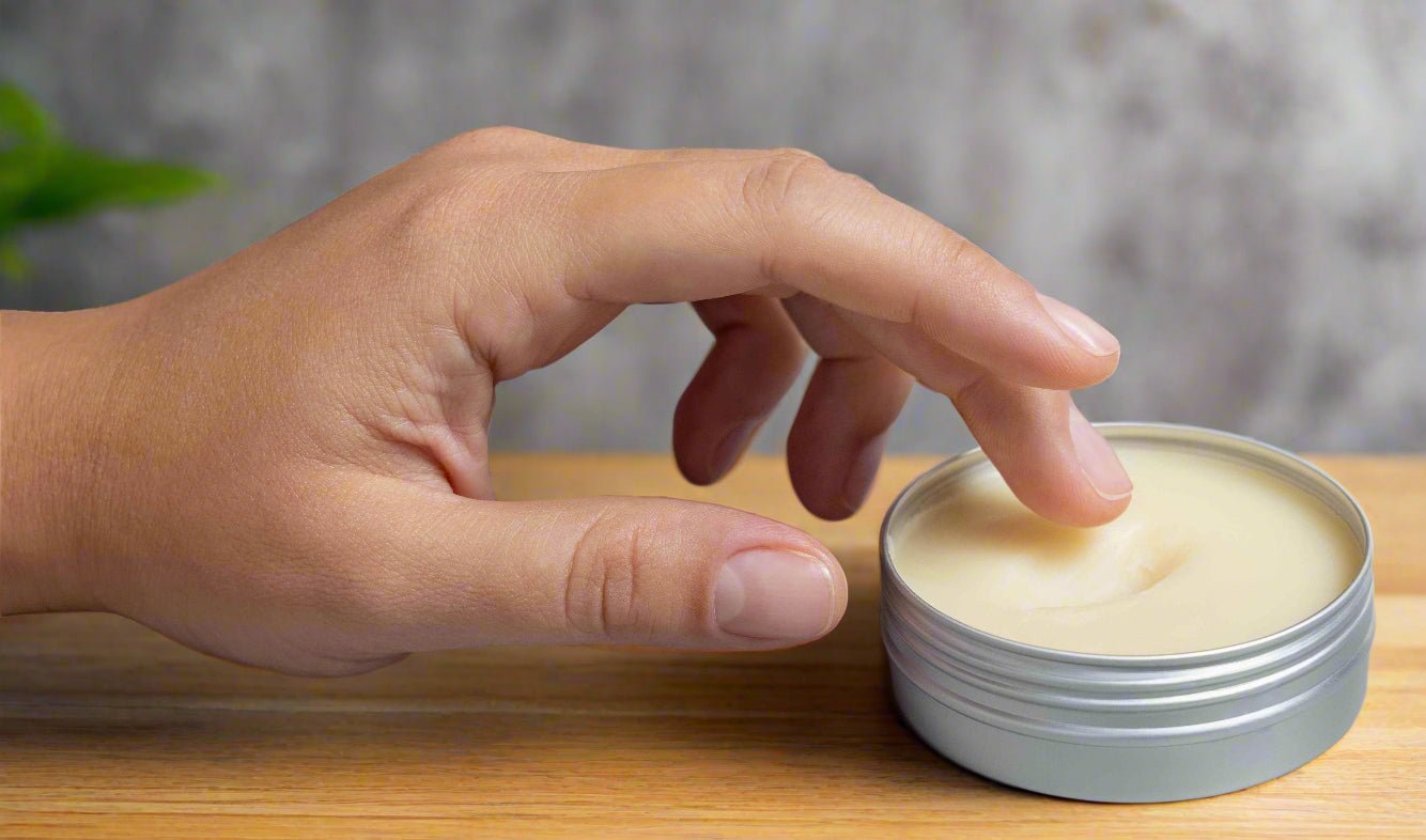 Hand applying cream from a small container on a wooden surface with a neutral background