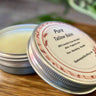 Open tin of Pure Tallow Balm with a visible label on a wooden surface.