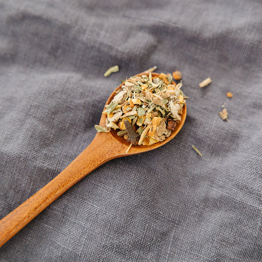 Wooden spoon filled with Organic Throat Soothe Tea By Bush Berry dried herbs on a gray fabric background