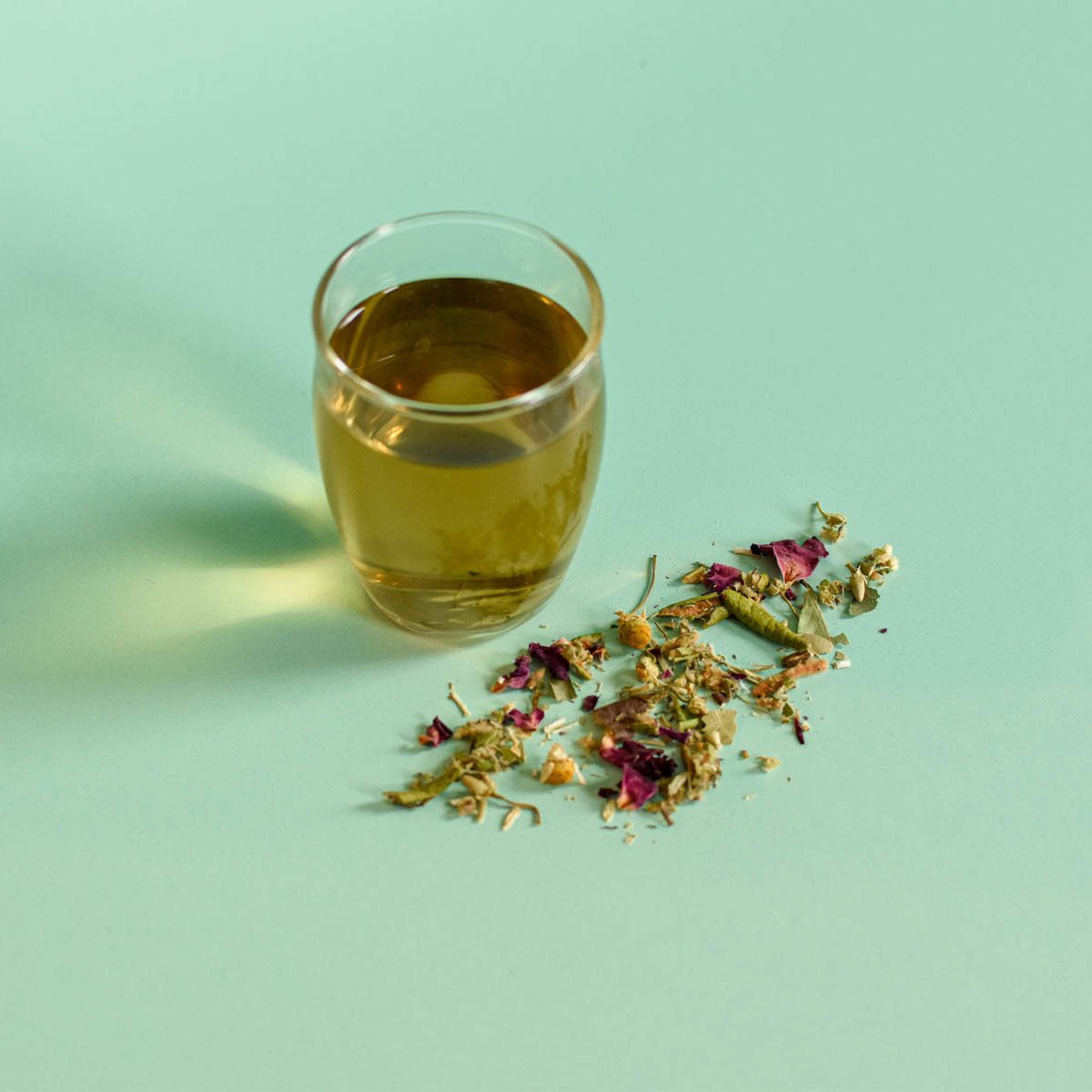 Glass of tea with dried herbs on a light green background Rose & Chamomile Loose Herbal Tea | Floèm
