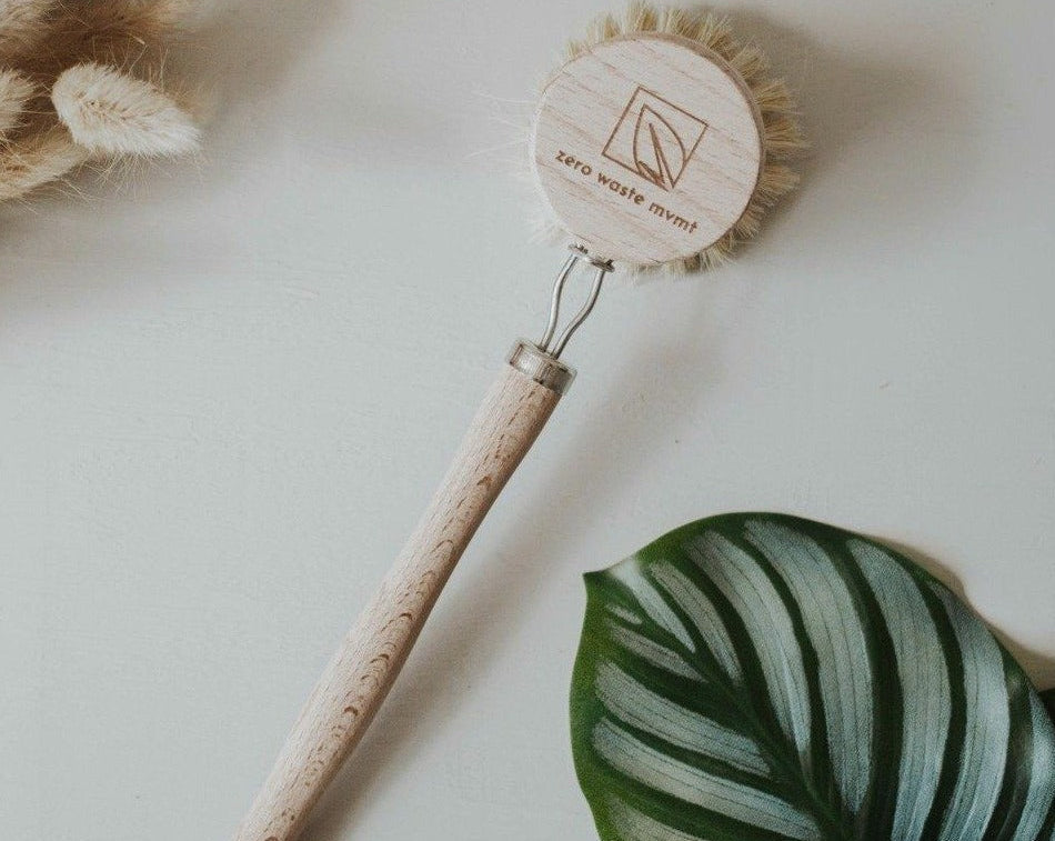Cleaning brush with cork handle and wooden bristle head on a light background with a leaf and dried plants.